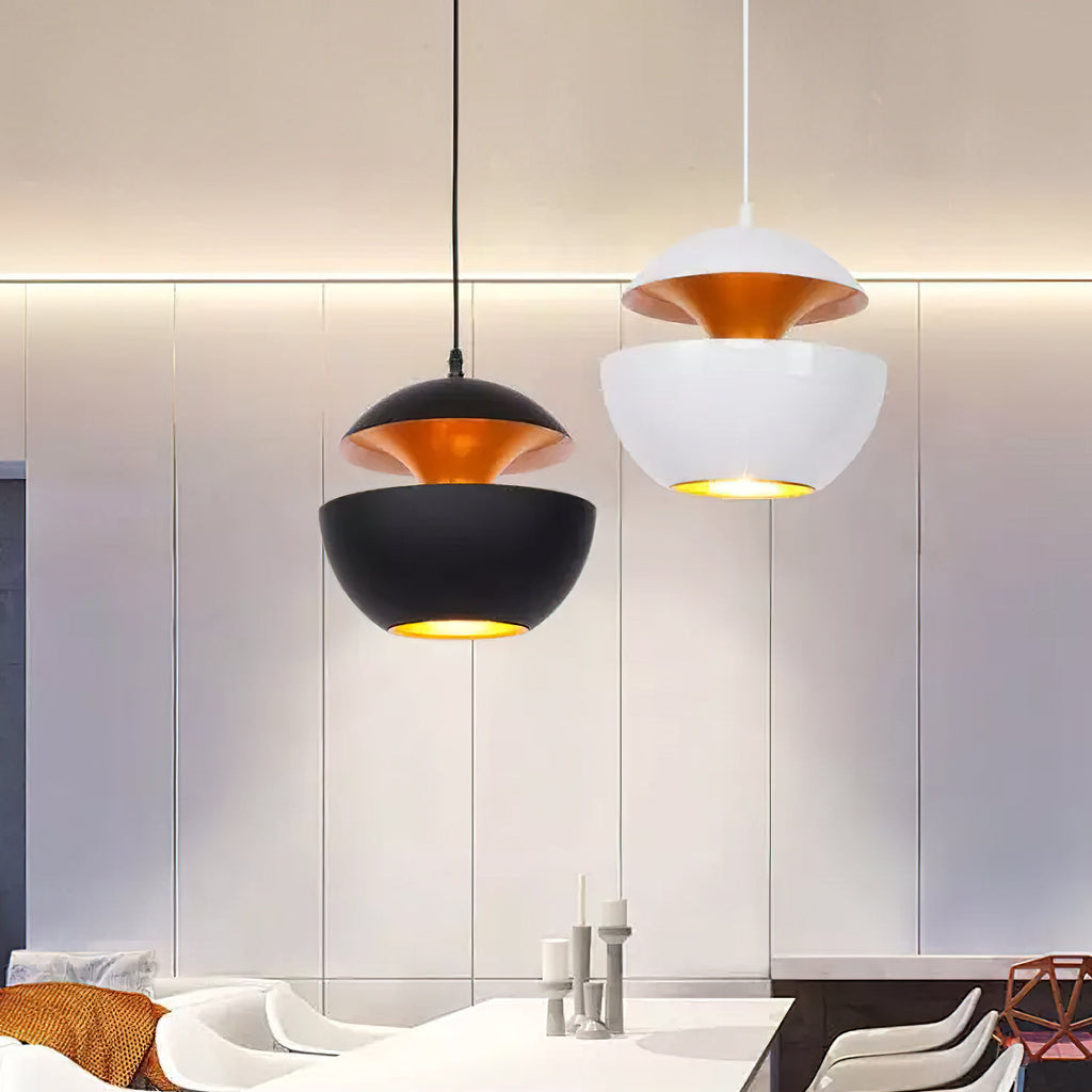 Black and white pendants with gold interiors above a white table and chairs, a Clérachic pair shown against a panelled wall.