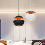 Black and white pendants with gold interiors above a white table and chairs, a Clérachic pair shown against a panelled wall.