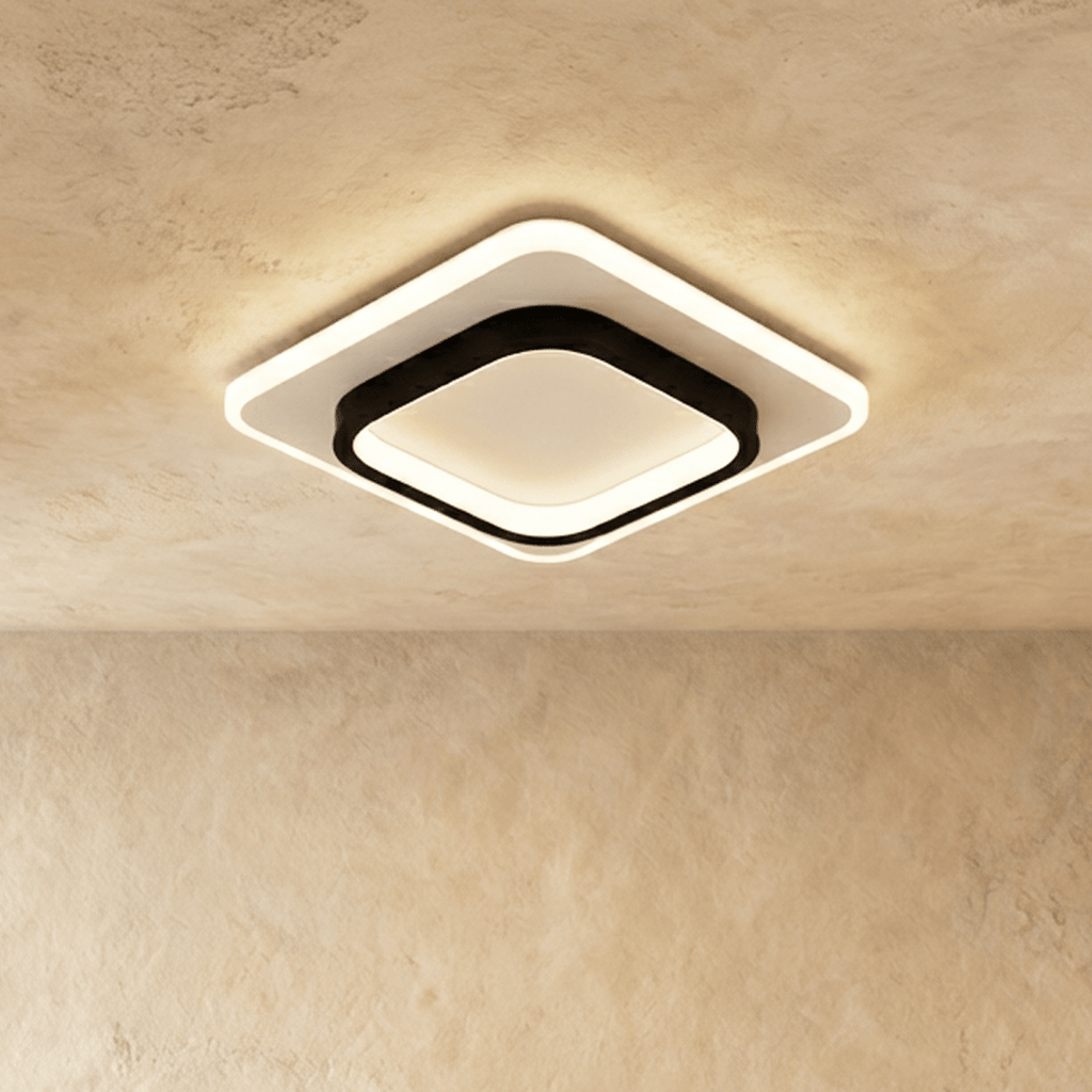 Clérachic rounded-square ceiling light with a black inner frame and white acrylic panel, glowing warm on a plastered ceiling.