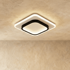 Clérachic rounded-square ceiling light with a black inner frame and white acrylic panel, glowing warm on a plastered ceiling.