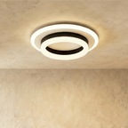 Clérachic two-tier round ceiling light with a black ring and frosted white acrylic rings, glowing warm on a limewash ceiling.