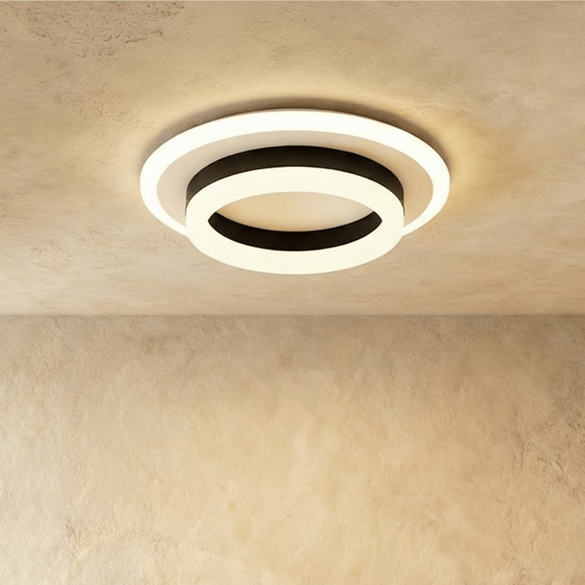 Clérachic two-tier round ceiling light with a black ring and frosted white acrylic rings, glowing warm on a limewash ceiling.
