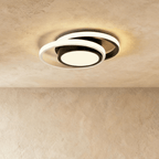 Clérachic ceiling light with two offset white rings around a black round core, glowing warm on a plastered ceiling.