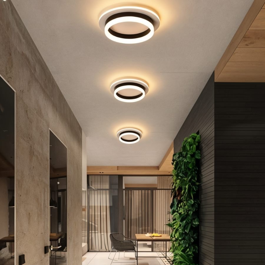 Three Clérachic round black and white ceiling lights in graduated sizes, lighting a corridor beside a concrete wall and plants.