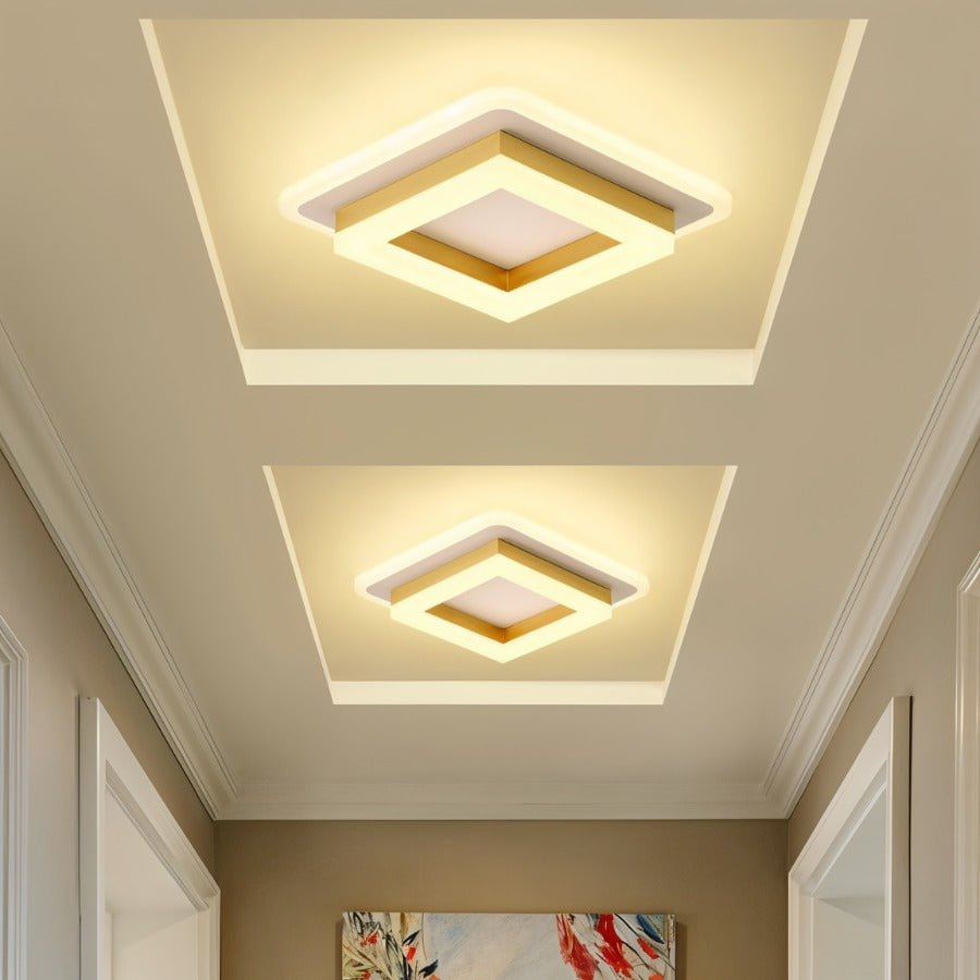 Two Clérachic square gold-finish ceiling lights in different sizes, glowing in recessed ceiling panels above a bright hallway.