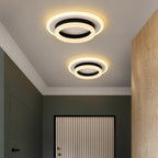 Two Clérachic round black and white ceiling lights in different sizes, glowing above a hallway with a green wall and oak panel.