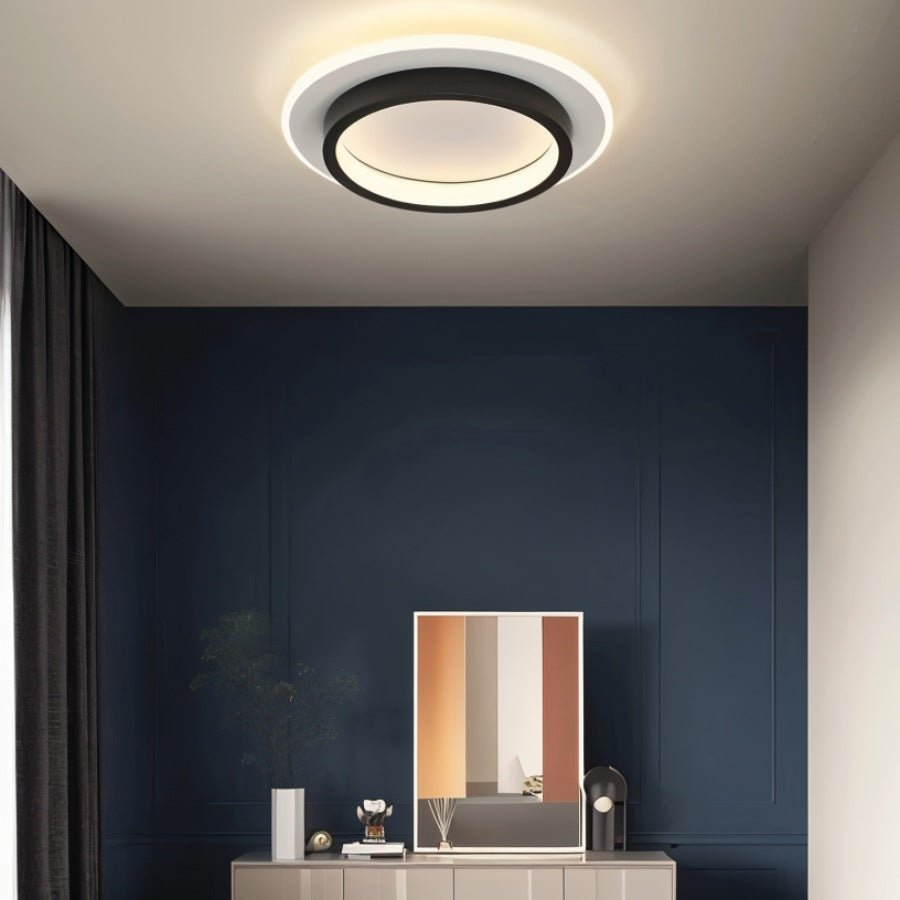 A Clérachic round black and white ceiling light glowing warm above a navy panelled wall, sideboard and framed print.