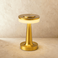 Clérachic cordless table lamp in brushed gold, a flat disc head over a glowing opal band, on a limewashed surface