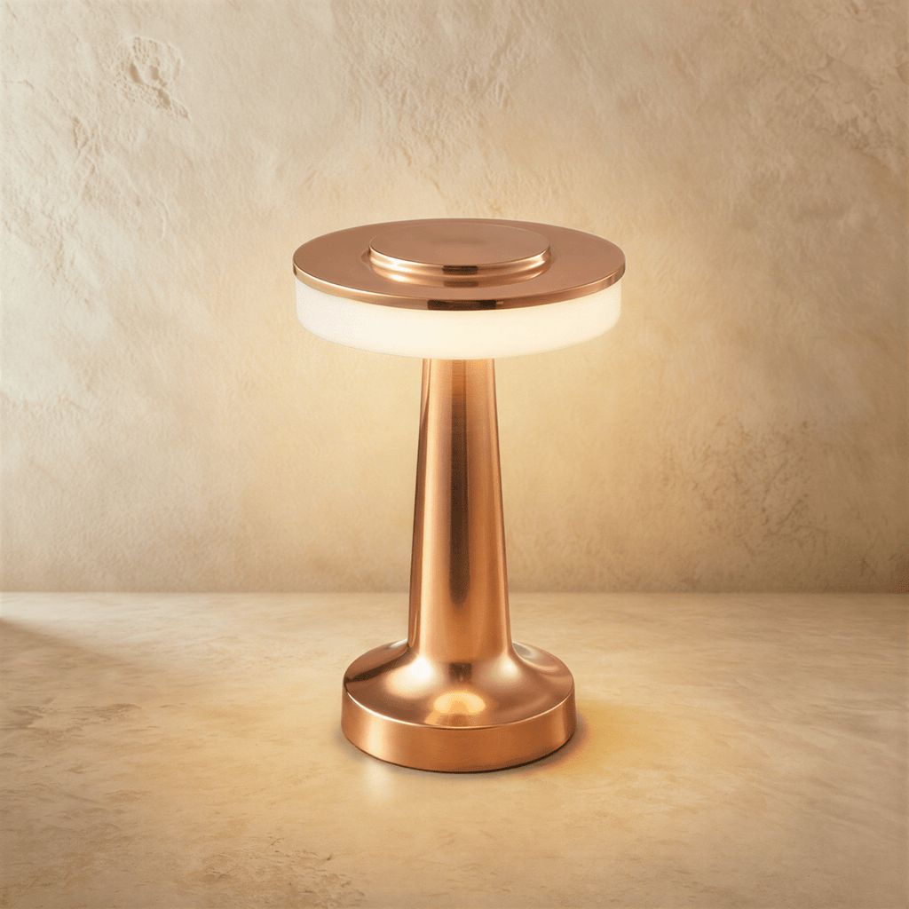 Clérachic cordless table lamp in polished rose gold, lit, its flat disc head above a softly glowing opal band