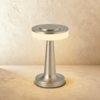 Clérachic cordless table lamp in satin silver, lit, a slim tapered stem rising from a round base to a disc head