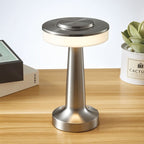 Clérachic cordless table lamp in brushed silver on a wooden desk beside books and a potted succulent, softly lit
