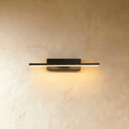 Clérachic black aluminium bar wall light, lit with a warm glow along its length, mounted on a textured limewash wall.
