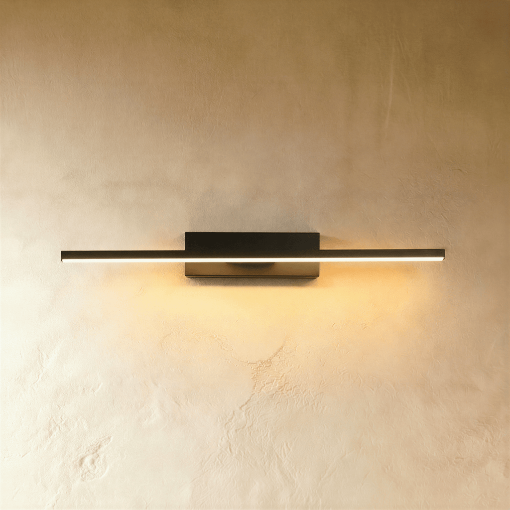 Clérachic longer black bar wall light glowing warm white against a soft limewash wall, arm centred on its backplate.