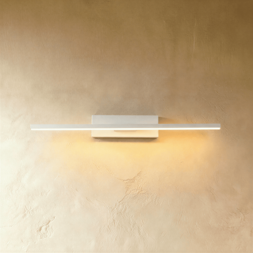 Clérachic mid-length white bar wall light with a warm lit arm, mounted on a plain white backplate against limewash.