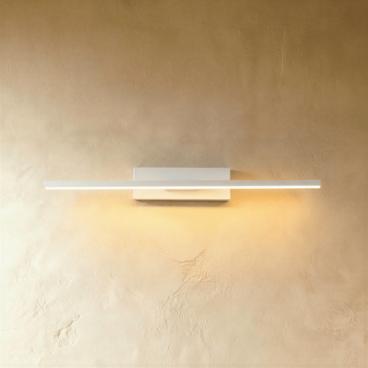 Clérachic mid-length white bar wall light with a warm lit arm, mounted on a plain white backplate against limewash.