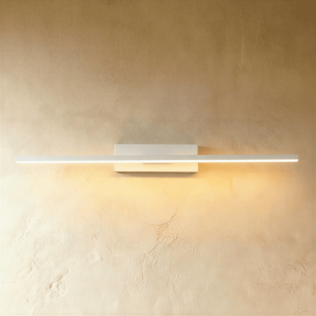 Clérachic long white bar wall light lit warm along its full length, on a rectangular backplate against a limewash wall.