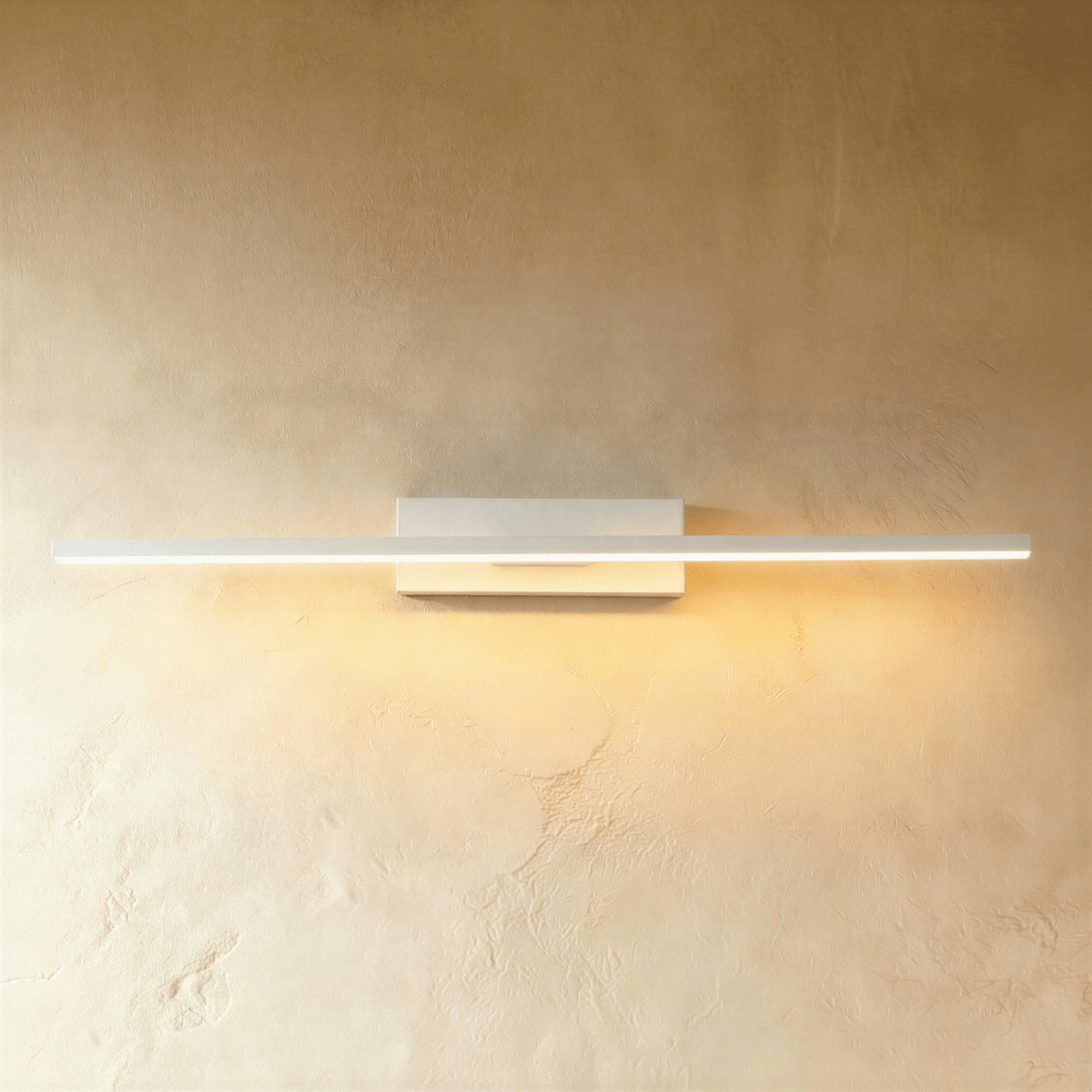 Clérachic long white bar wall light lit warm along its full length, on a rectangular backplate against a limewash wall.