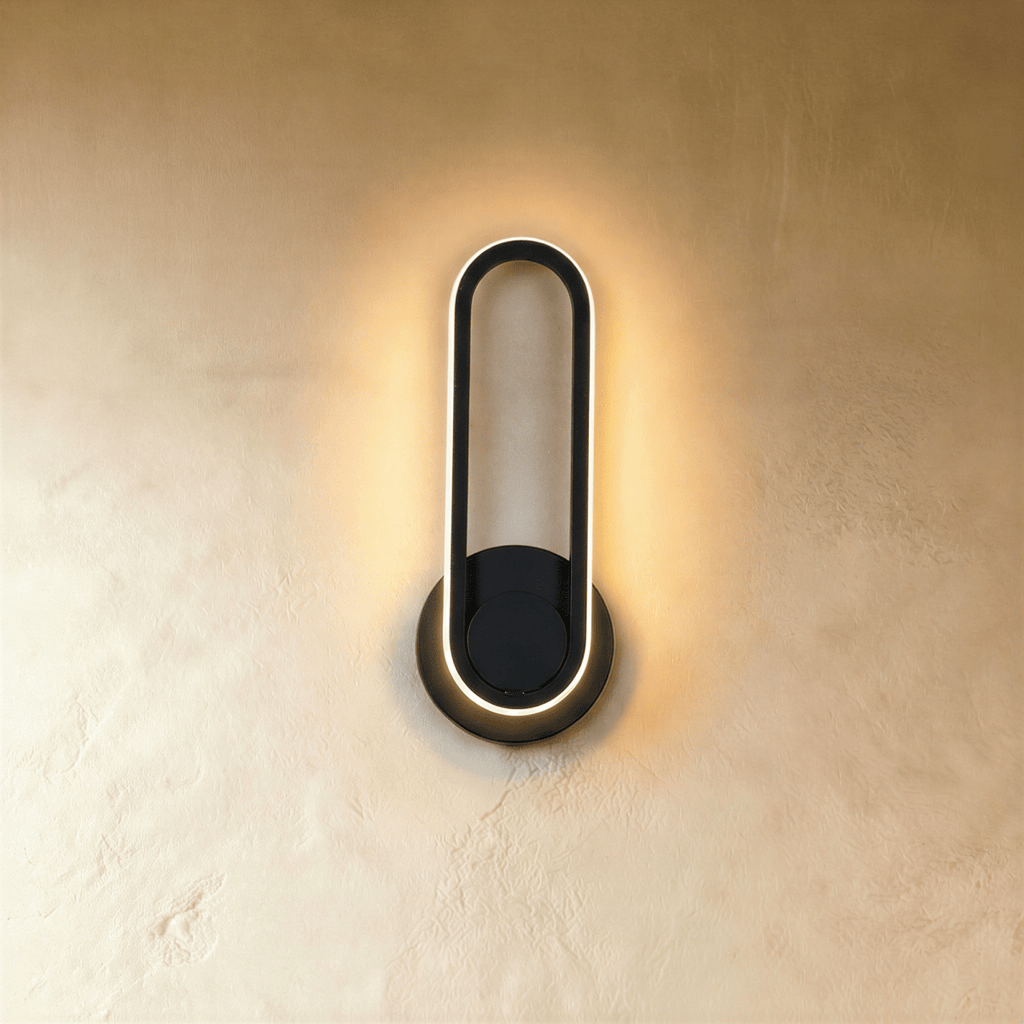 Clérachic black oval ring wall light with a warm glowing edge on a round backplate, hung on a limewash wall.