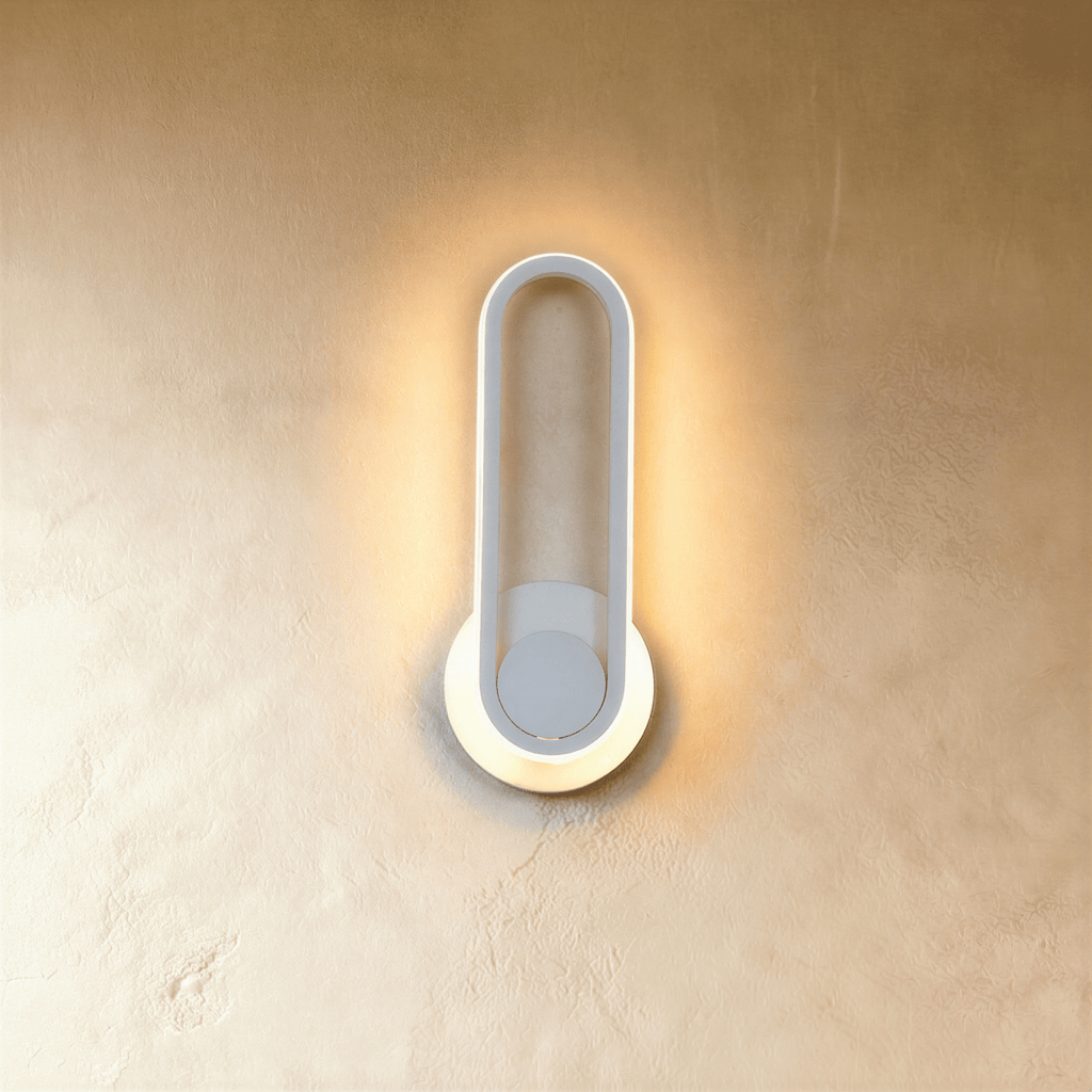 Clérachic white oval ring wall light, its edge glowing warm over a round white backplate on a limewash wall.