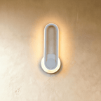 Clérachic white oval ring wall light, its edge glowing warm over a round white backplate on a limewash wall.