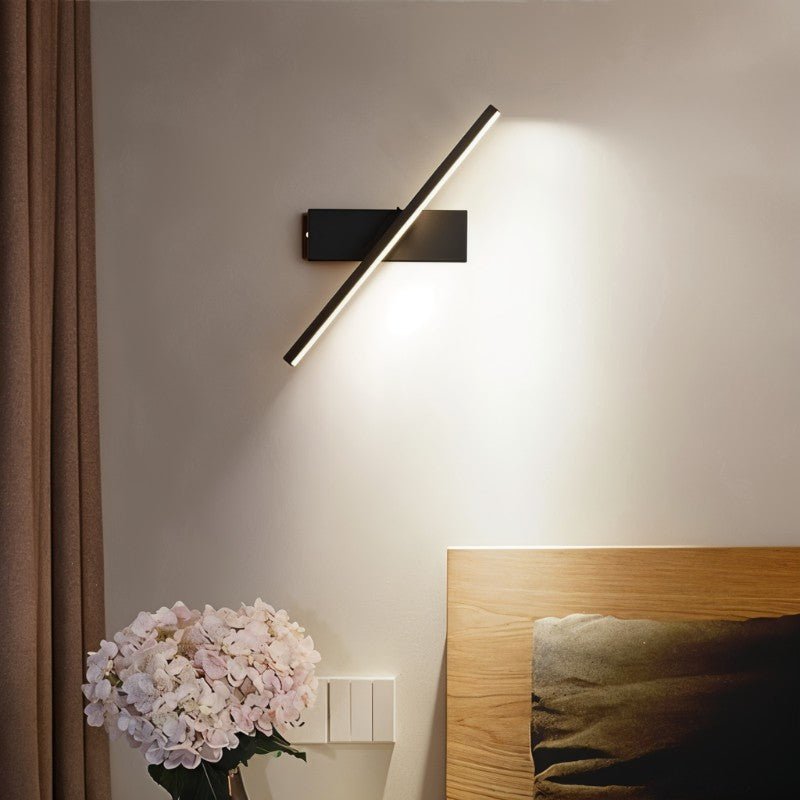 Clérachic black bar wall light swung to a diagonal beside a bed, washing the wall with soft light above hydrangeas.