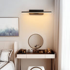 Clérachic black bar wall light mounted above a dressing table and round mirror in a calm bedroom, casting a warm wash down the wall.