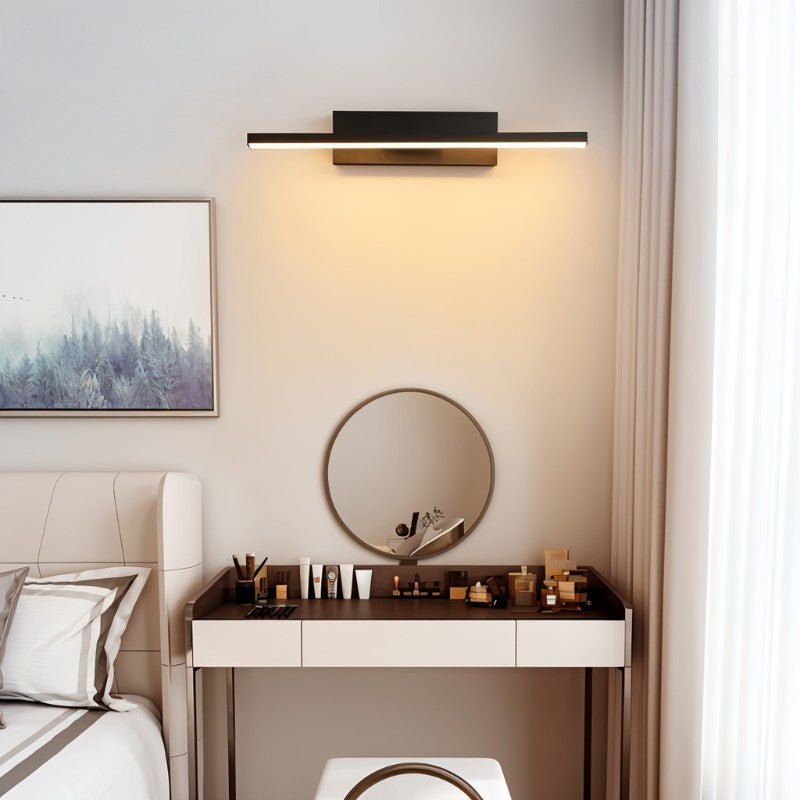Clérachic black bar wall light mounted above a dressing table and round mirror in a calm bedroom, casting a warm wash down the wall.