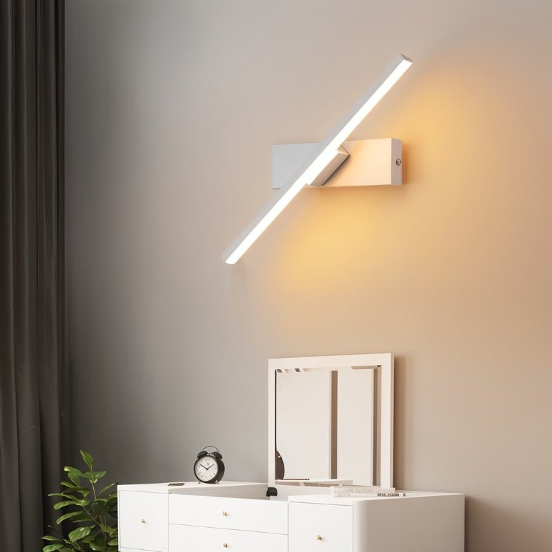 Clérachic white bar wall light angled diagonally above a white chest of drawers, throwing warm light across the wall.