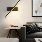 Clérachic black bar wall light angled steeply above a side table and grey sofa, giving a soft glow in a living room.
