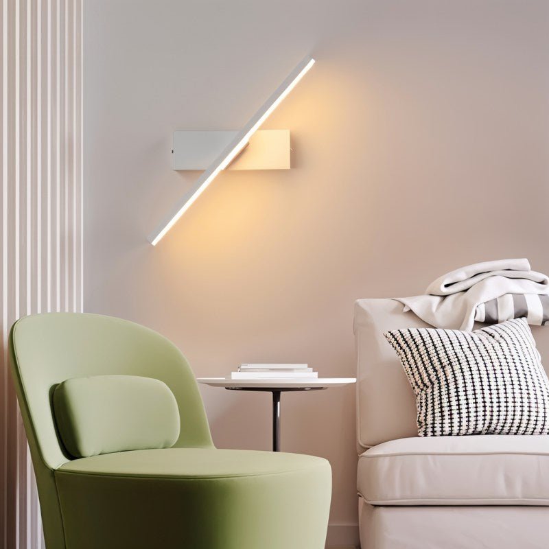 Clérachic white bar wall light rotated diagonally beside a green armchair and cream sofa, casting a warm glow on the wall.