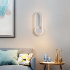 Clérachic white oval ring wall light glowing softly above a grey sofa and a round side table with gold candlesticks.