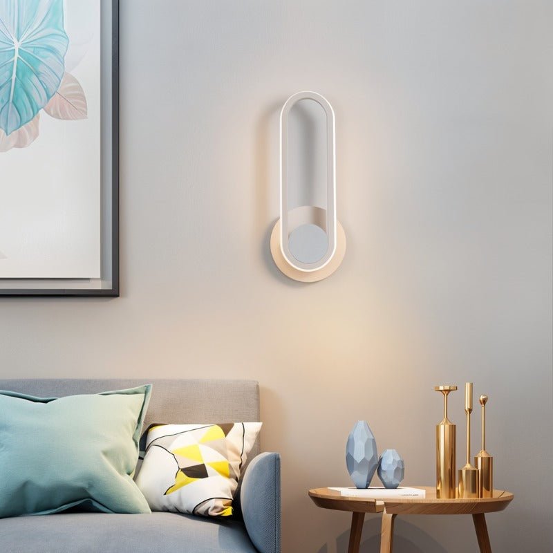 Clérachic white oval ring wall light glowing softly above a grey sofa and a round side table with gold candlesticks.