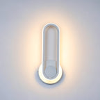 Clérachic white oval ring wall light close up, lit warm around its edge with a halo of light on a pale grey wall.