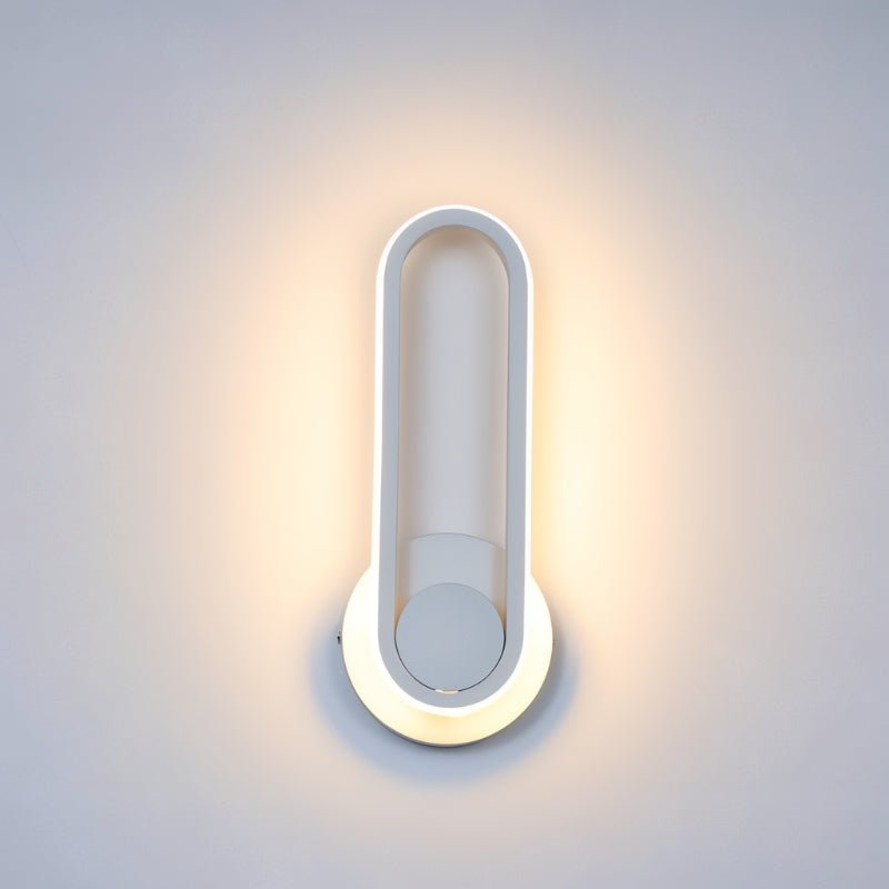 Clérachic white oval ring wall light close up, lit warm around its edge with a halo of light on a pale grey wall.