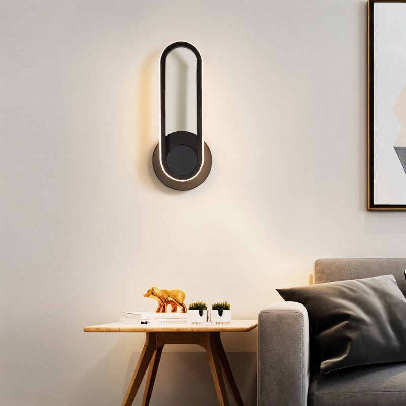 Clérachic black oval ring wall light with a warm lit edge, hung above a wooden side table and grey sofa.