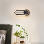 Clérachic black oval ring wall light turned horizontal above a side table of succulents, beside a dark green armchair.
