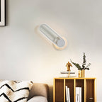 Clérachic white oval ring wall light tilted on its round plate above a wooden shelf unit with books and eucalyptus.
