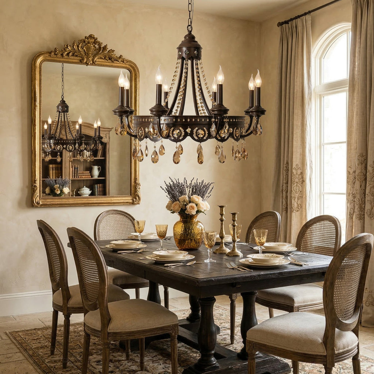 Clérachic chandelier with amber crystal drops hanging over a dark dining table, beside a gilt mirror and tall arched windows.