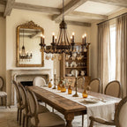 Clérachic bronze-finish chandelier above a long rustic dining table in a beamed room with a stone fireplace.