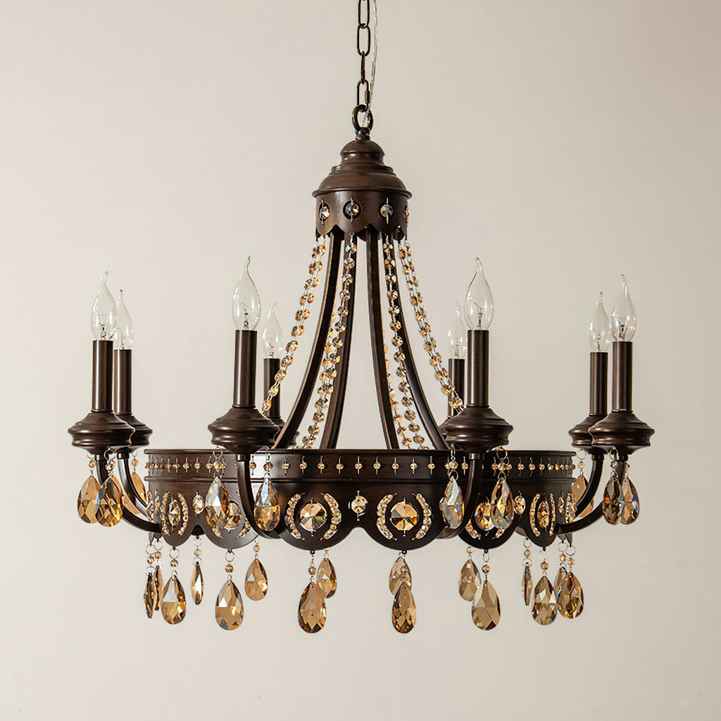 A Clérachic chandelier hung on a black chain, its candle bulbs and amber crystal drops lit against a pale wall.