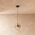 Clérachic glass cylinder pendant light with a brass midi band, hanging on a black cord from a round ceiling plate against a plastered wall.