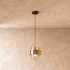 Clérachic glass cylinder pendant light with a brass midi band, hanging on a black cord from a round ceiling plate against a plastered wall.