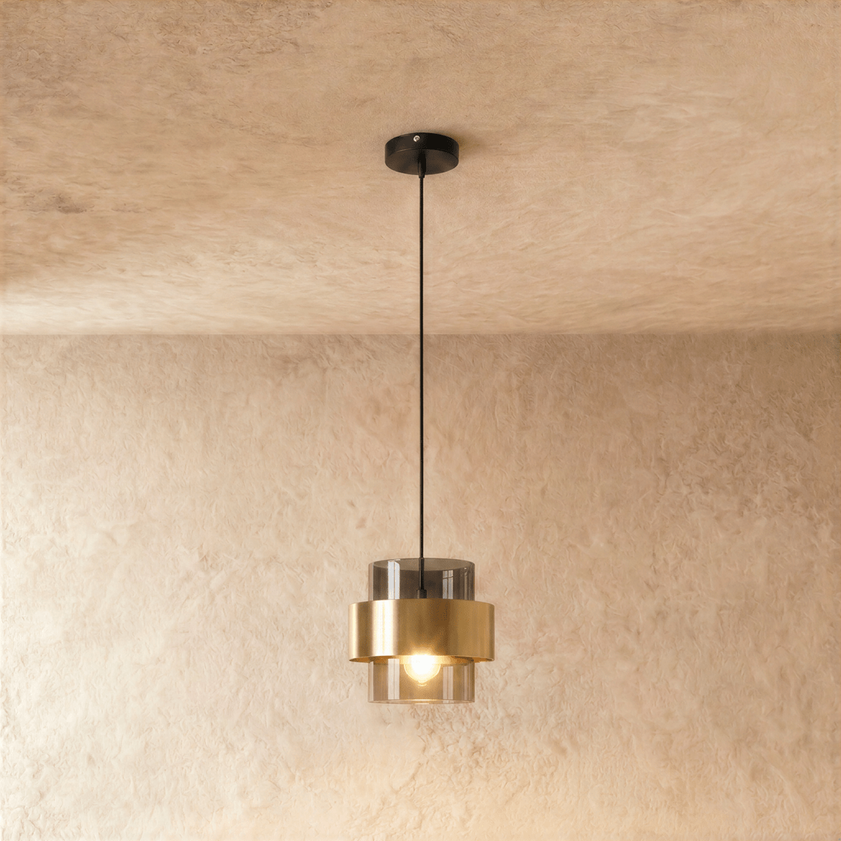 The Clérachic pendant in smoky gray glass with a brass band, hanging from a black cord against a soft plaster wall.