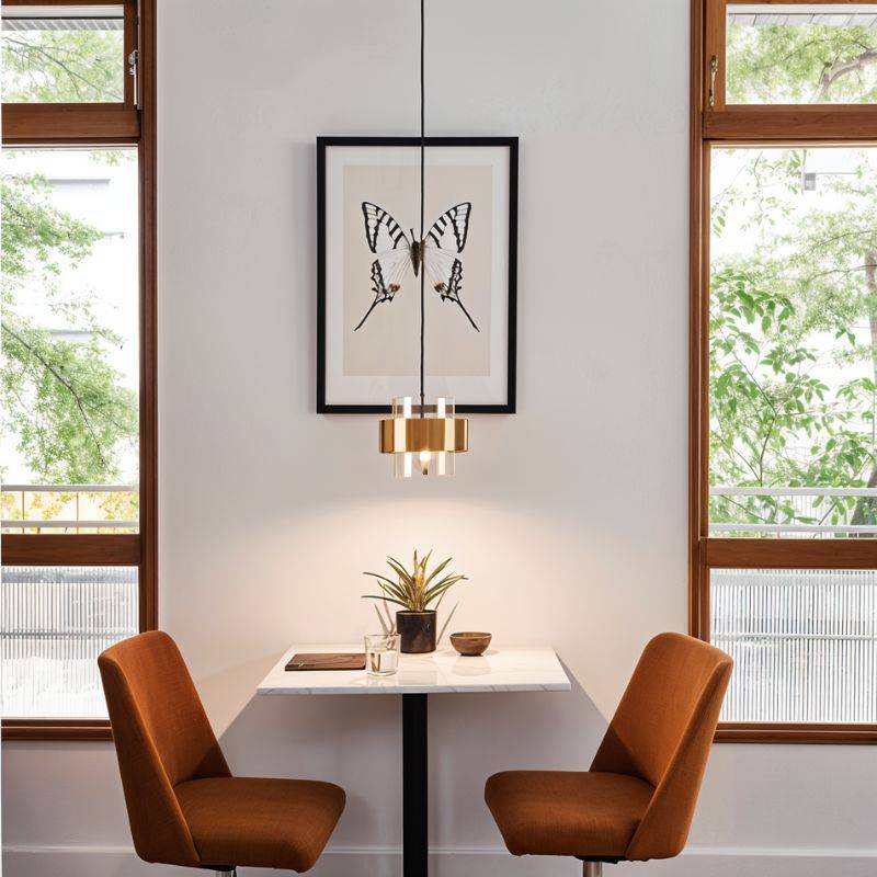 The Clérachic brass-banded pendant light hanging in front of a framed print, lighting a small dining table below.