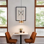 The Clérachic brass-banded pendant light hanging in front of a framed print, lighting a small dining table below.