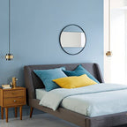 Two Clérachic cylinder pendants with brass bands hanging beside a grey upholstered bed in a blue-walled bedroom.