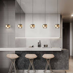 Five Clérachic cylinder pendants with brass bands hanging in a row above a marble-topped kitchen island bar.