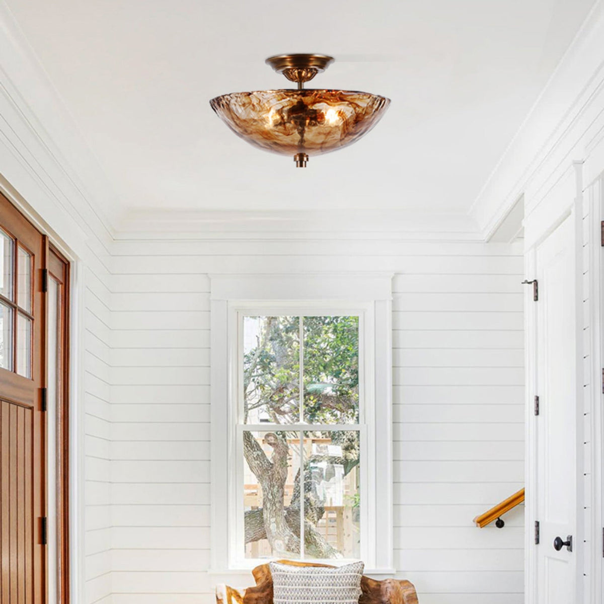 Hung in a white-panelled entrance hall, this Clérachic ceiling light shows its amber glass bowl glowing beside a window and a timber door.
