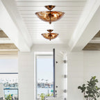 Two of these Clérachic ceiling lights hang one behind the other from a white beamed ceiling, looking out towards a glazed door and a harbour.