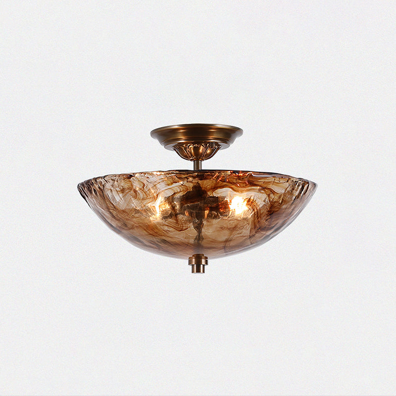This Clérachic ceiling light seen from slightly below on a pale backdrop, its bronze stem and canopy rising above the lit amber glass bowl.